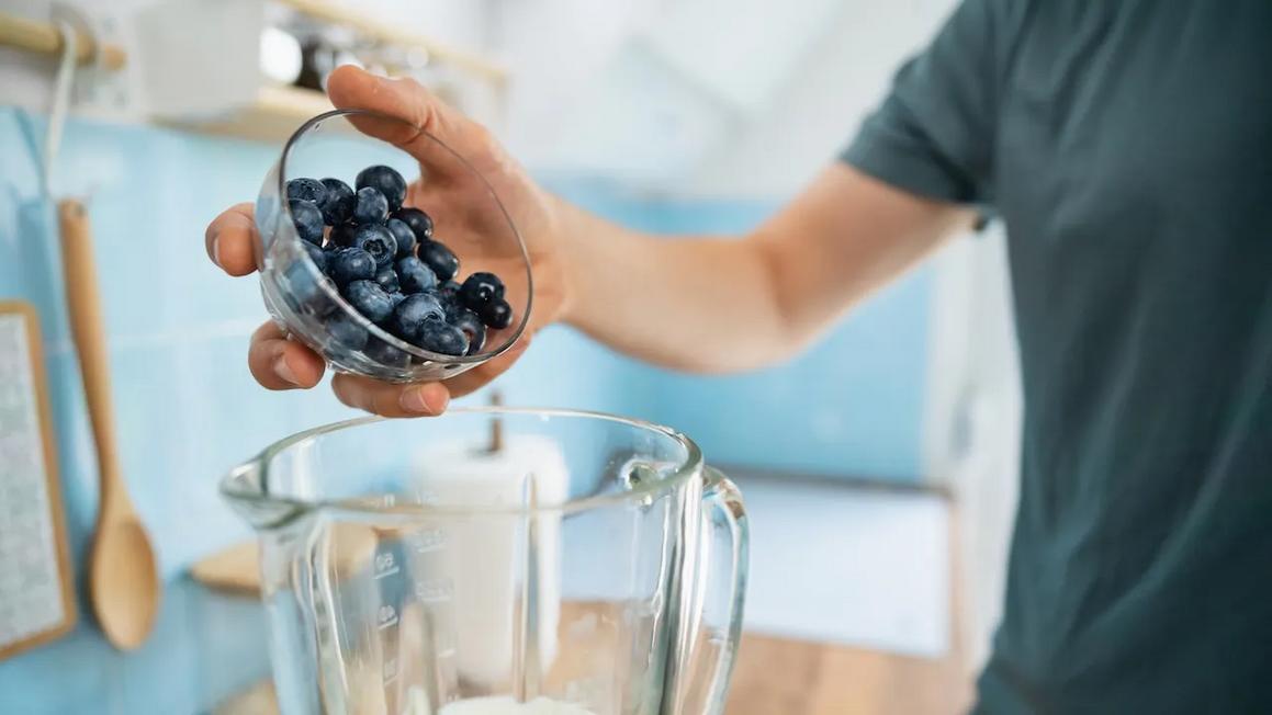 man putting blueberries in blender