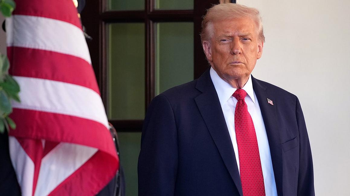 trump stands next to flag