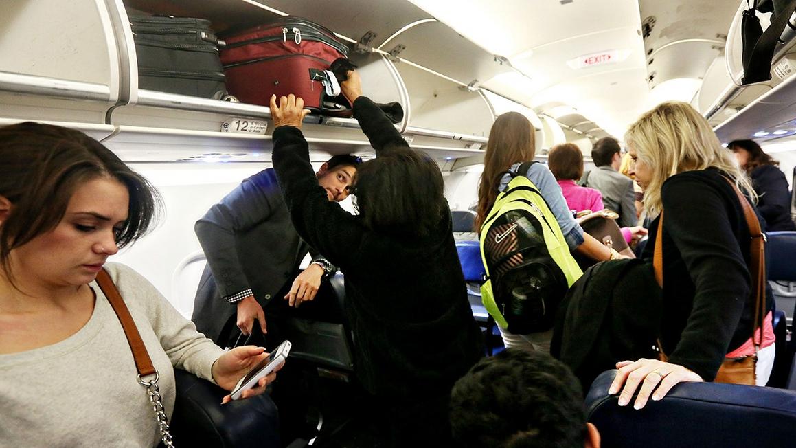 woman puts bag overhead bin airport